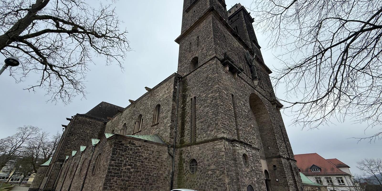 Große Kirche aus Naturstein mit markantem Turm, aufgenommen von einem gepflasterten Vorplatz.