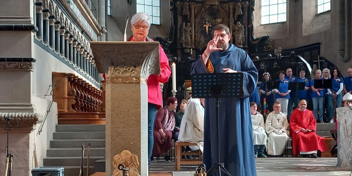 Person liest am Ambo, während eine weitere Person in Gebärdenchor-Gewand Gebärden für die Gemeinde übersetzt.