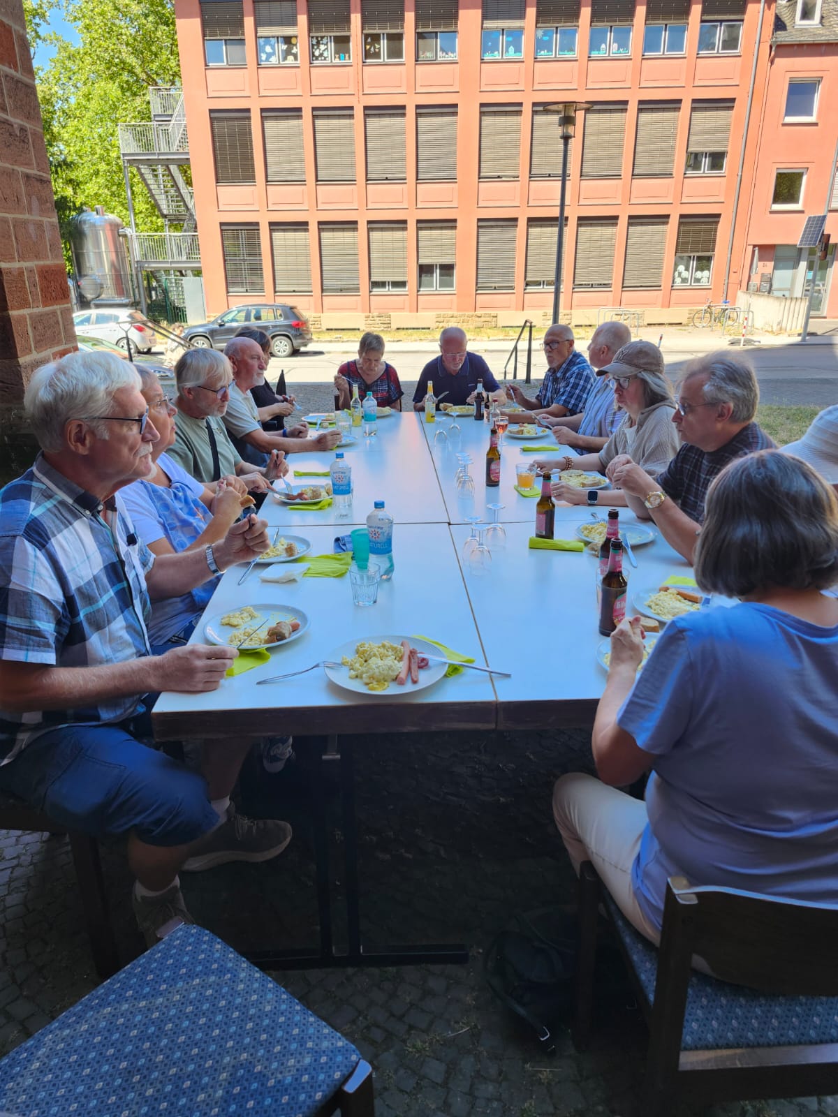 Gemeinsames Essen an einer langen Tafel im Freien, neben der Kirche und hinten die Straße.