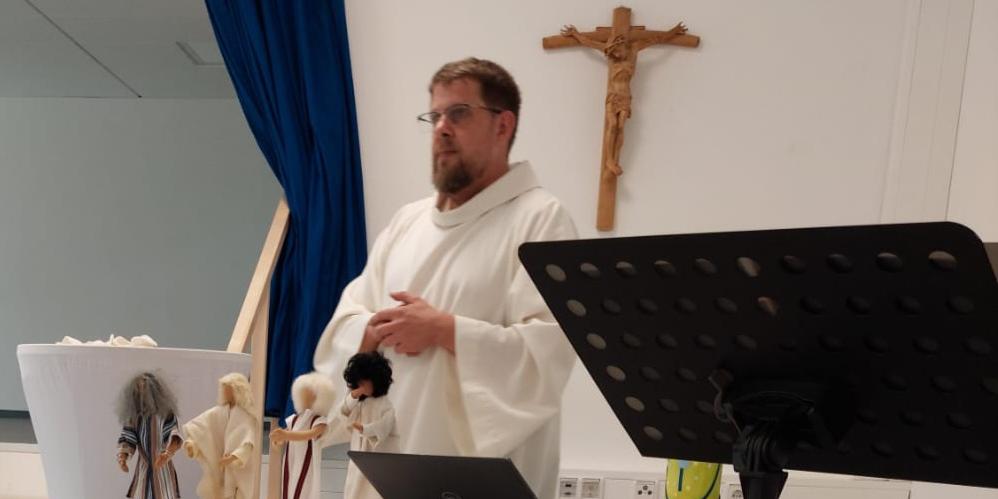 Altar Pfarrsaal Person in liturgischer Kleidung präsentiert vor einem Tisch mit biblischen Darstellungen und Kruzifix.