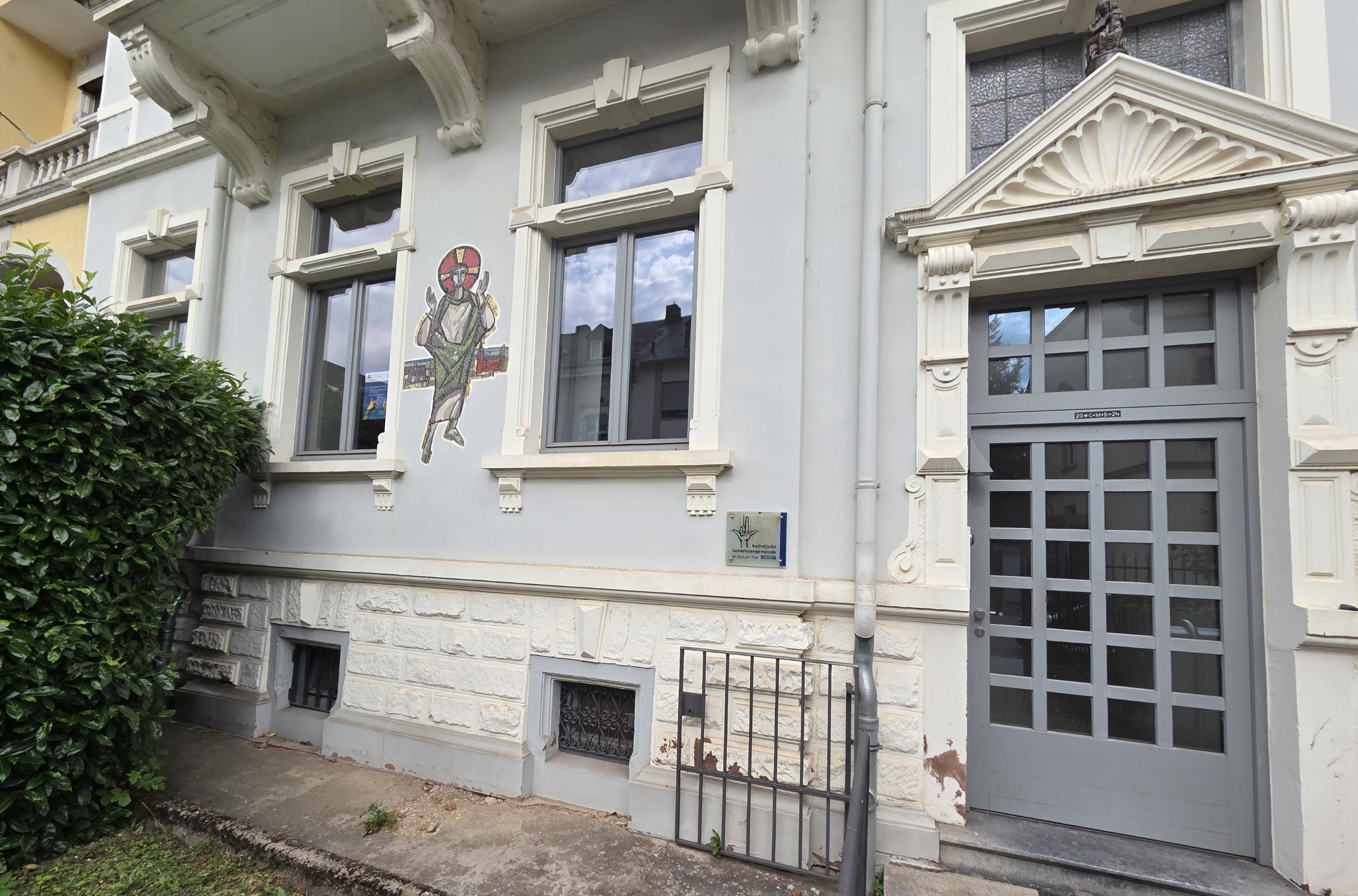 Eingang eines historischen Gebäudes mit Hinweisschild und Wandbild an der Fassade.