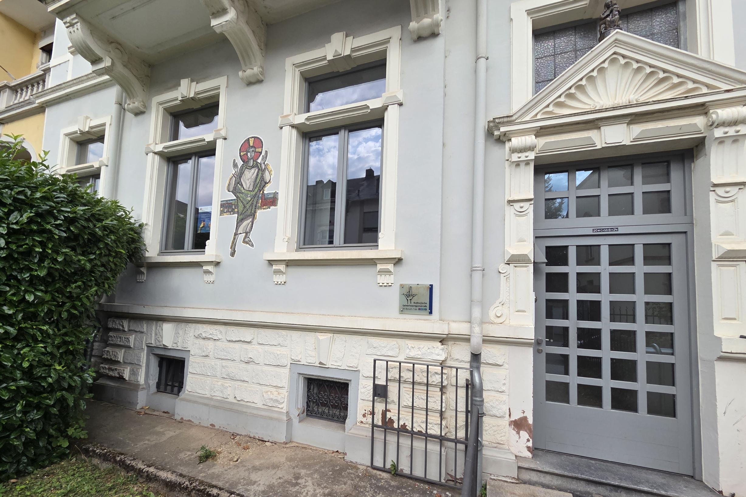 Eingang eines historischen Gebäudes mit Hinweisschild und Wandbild an der Fassade.