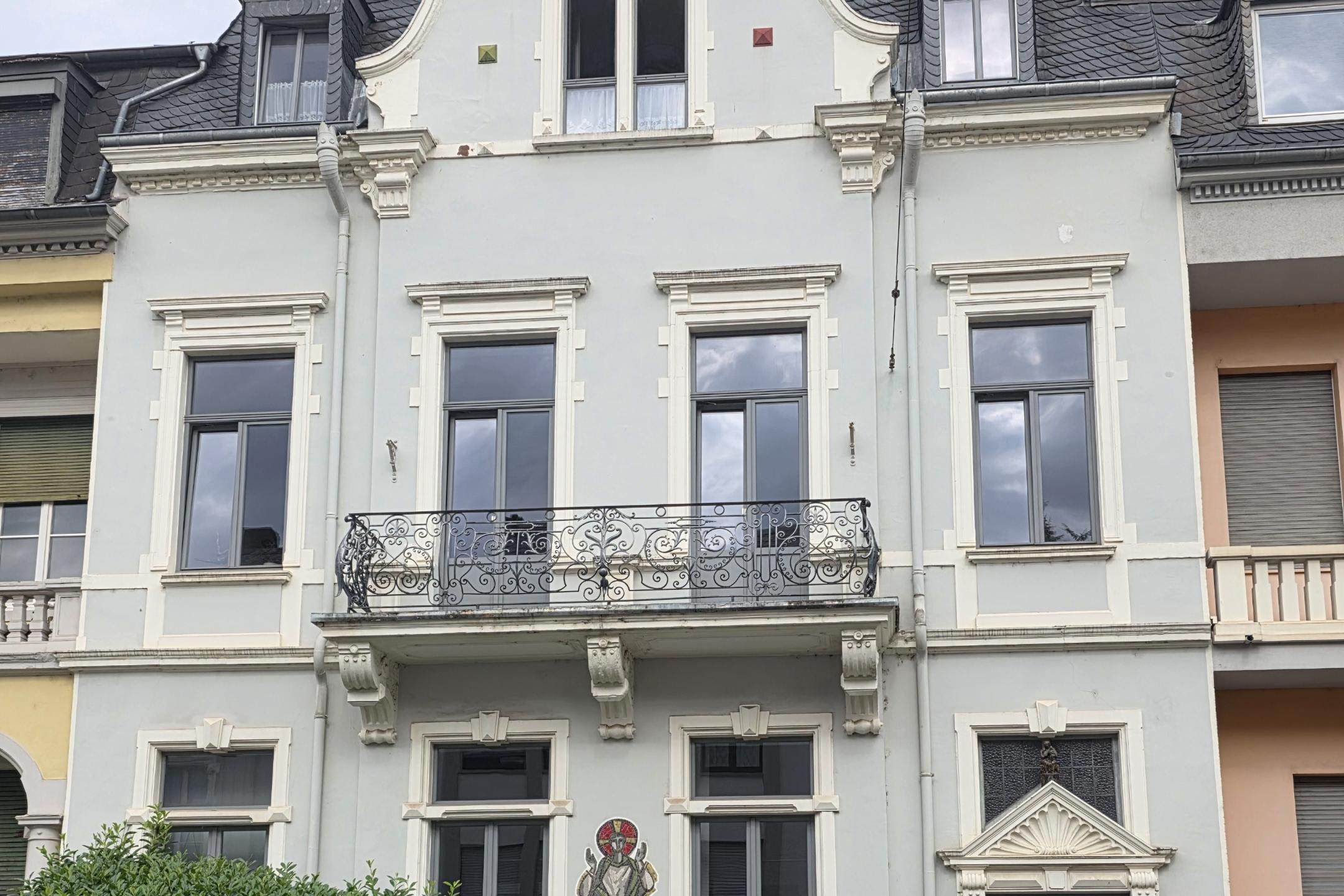 Historisches Wohnhaus mit heller Fassade, Balkon und verzierten Fenstern in einer Häuserzeile.