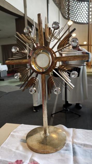 Monstranz mit Hostie auf dem Altar; im Hintergrund stehen liturgische Dienste im Kirchenraum.