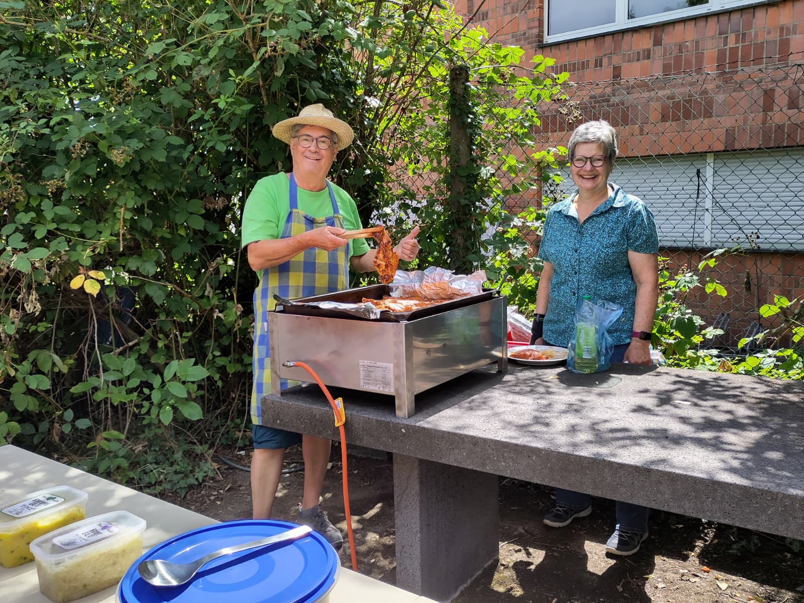 Zwei Personen bereiten an einem Grill im Freien Essen zu und präsentieren gegrillte Speisen für ein Grillfest.