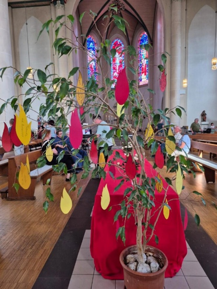 Baum mit roten und gelben Papierflammen als Pfingstsymbol im Mittelgang einer Kirche.