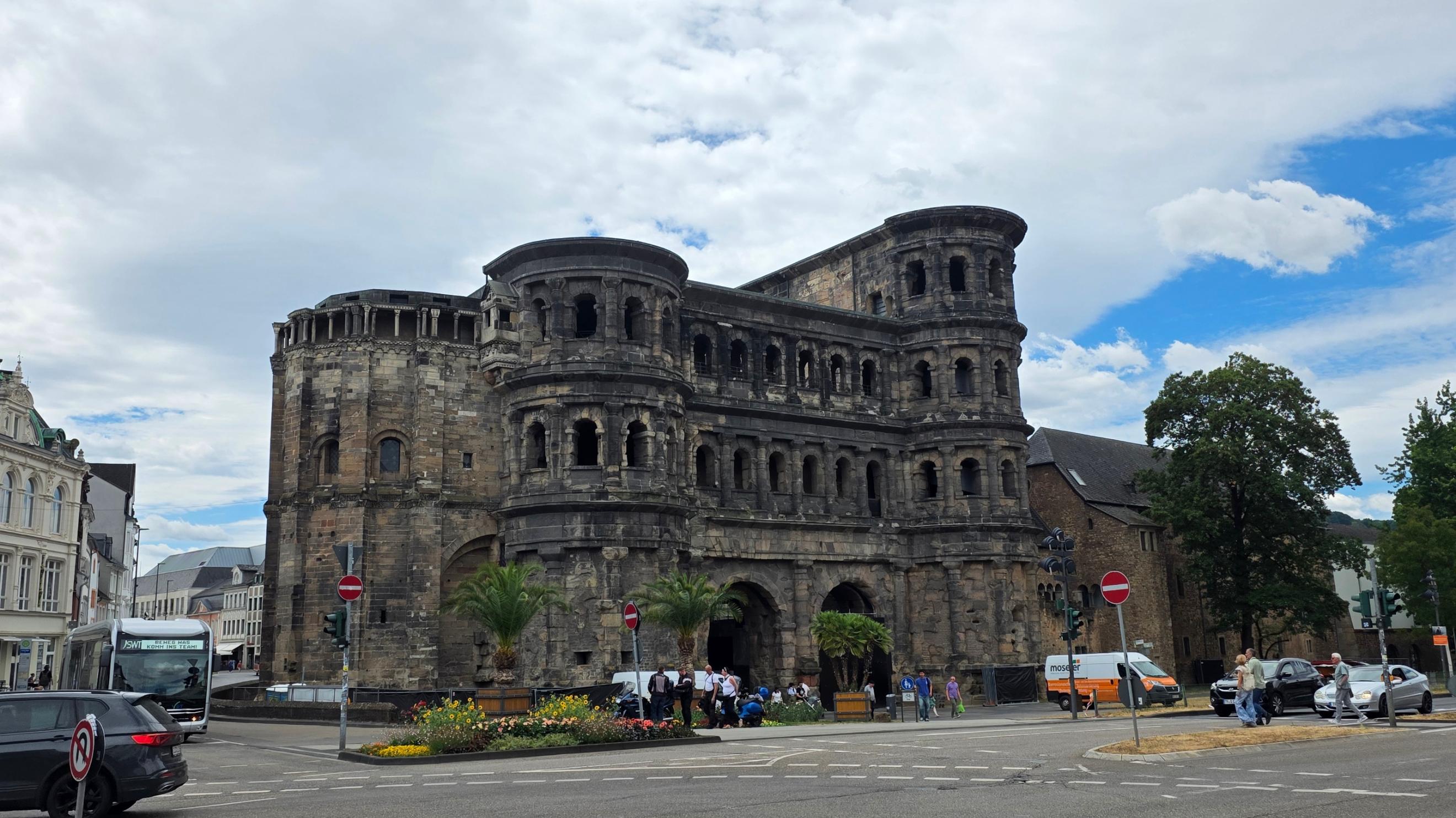 Die Porta Nigra in Trier, ein großes römisches Stadttor aus dunklem Stein, an einer Straßenkreuzung. (c) Daniel Beinhoff Die Porta Nigra in Trier, ein großes römisches Stadttor aus dunklem Stein, an einer Straßenkreuzung.