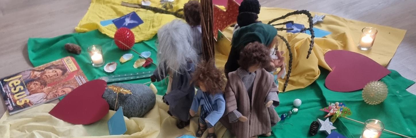 Bodenbild mit Kerze, Figuren, Herzen und Glaubenssymbolen zur gemeinsamen Andacht oder Gruppenarbeit.