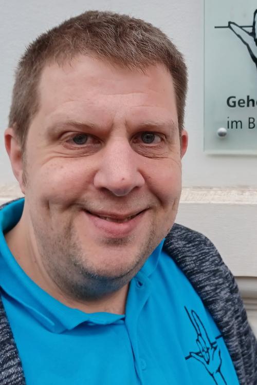 Porträt einer Person vor einer Informationswand der Gehörlosenseelsorge im Bistum Trier.