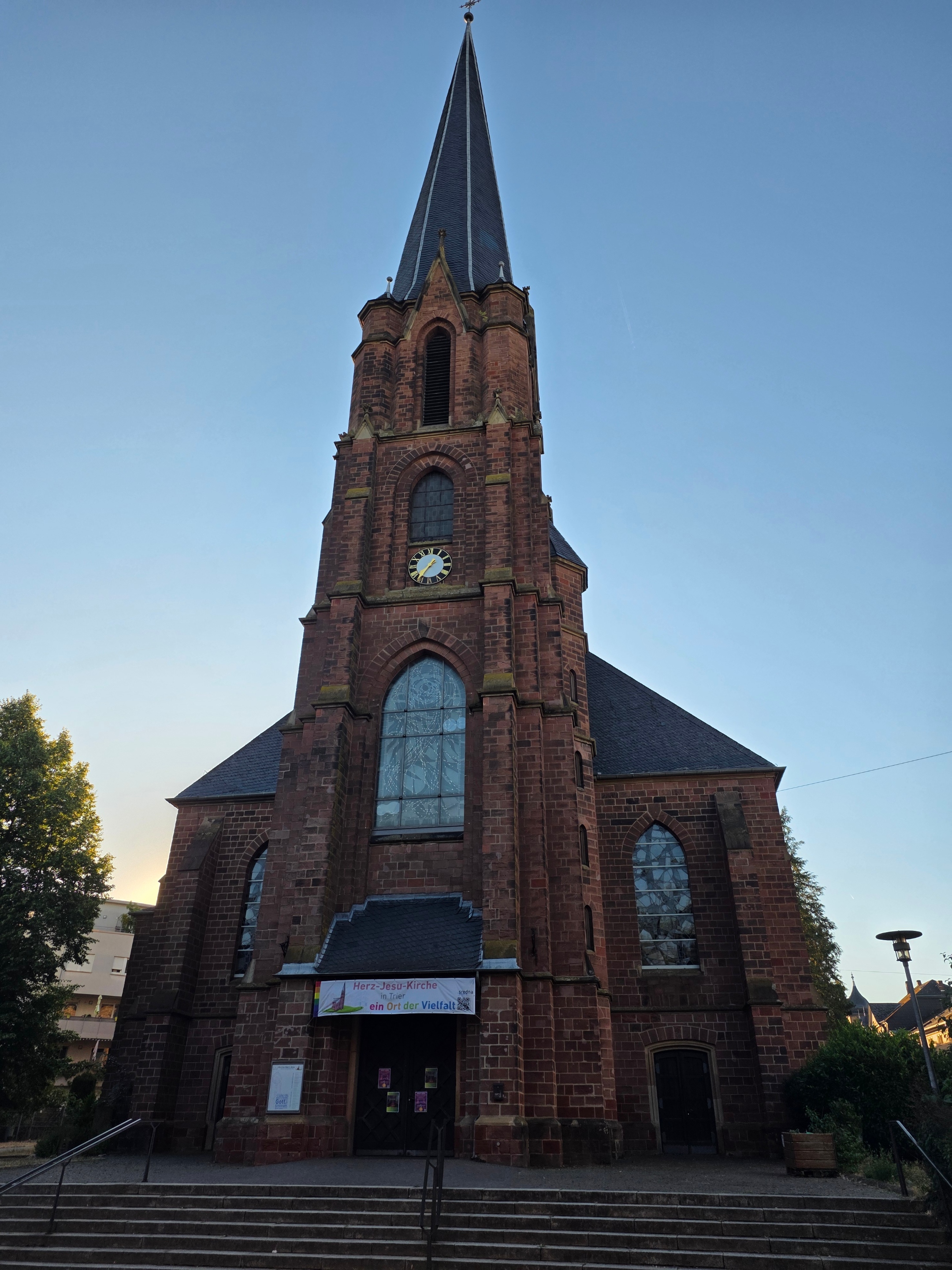 Kirchenfassade mit hohem Turm, großen Spitzbogenfenstern und Eingang über mehrere Treppenstufen