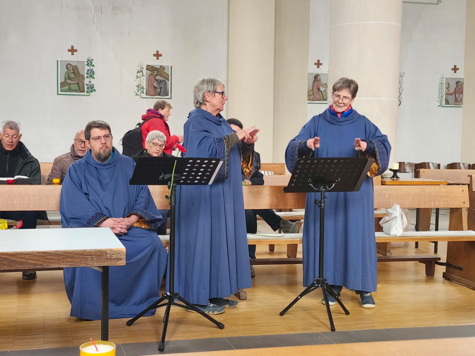 Drei Mitwirkende in blauen Gewändern gebärden einen Lied.