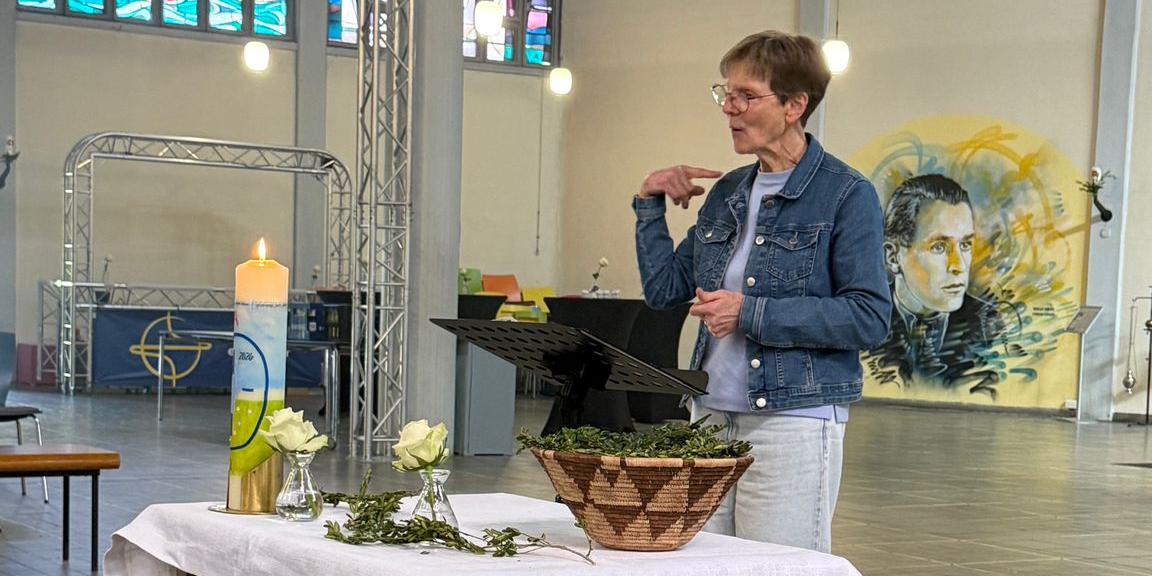 Person gebärdet am Lesepult neben einem Tischaltar; die Gemeinde sitzt im Kirchenraum.