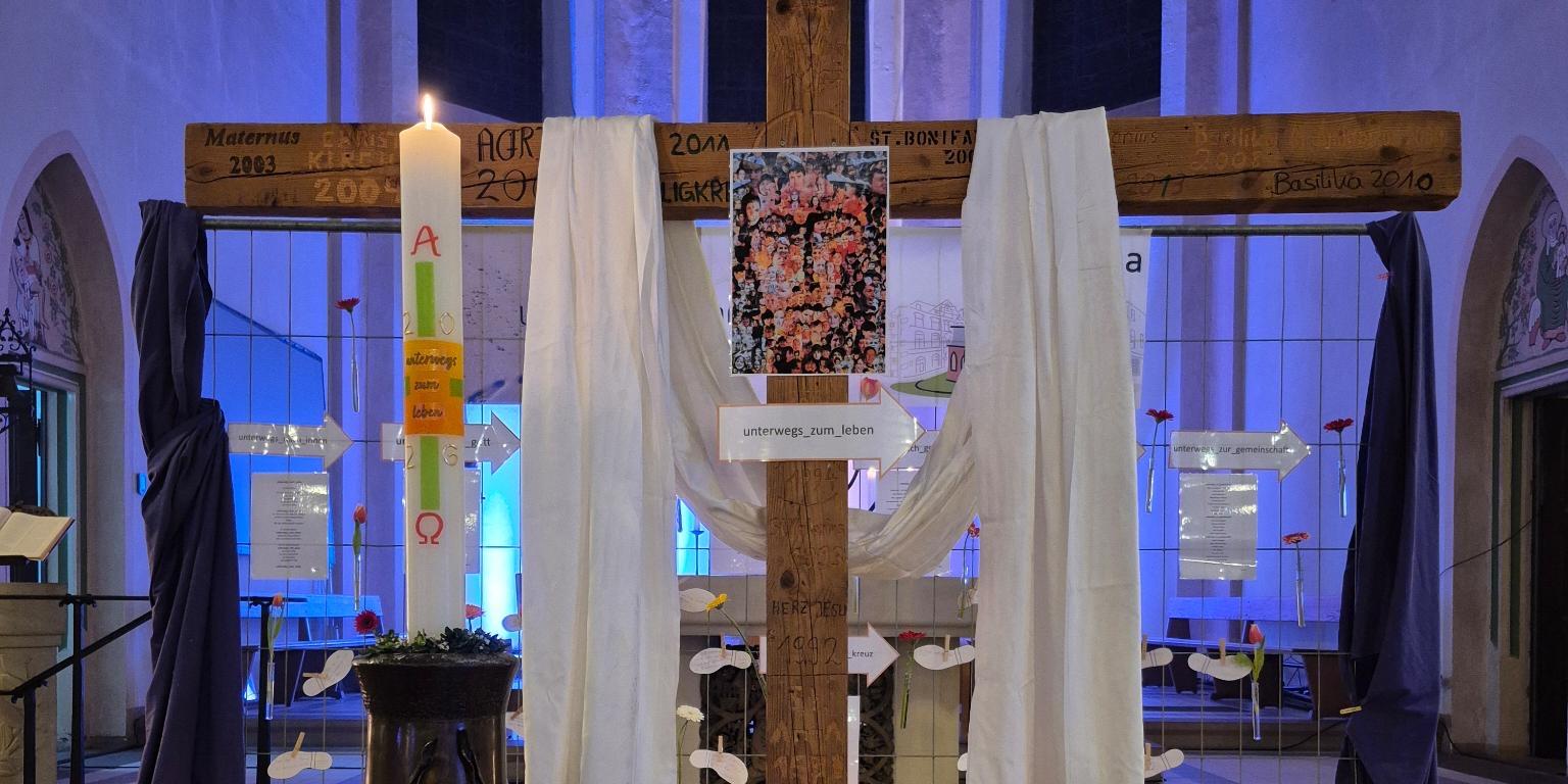 Mit weißen Tüchern verhülltes Kreuz im Altarraum, davor Osterkerze, Bibel und Symbole der Passionszeit.