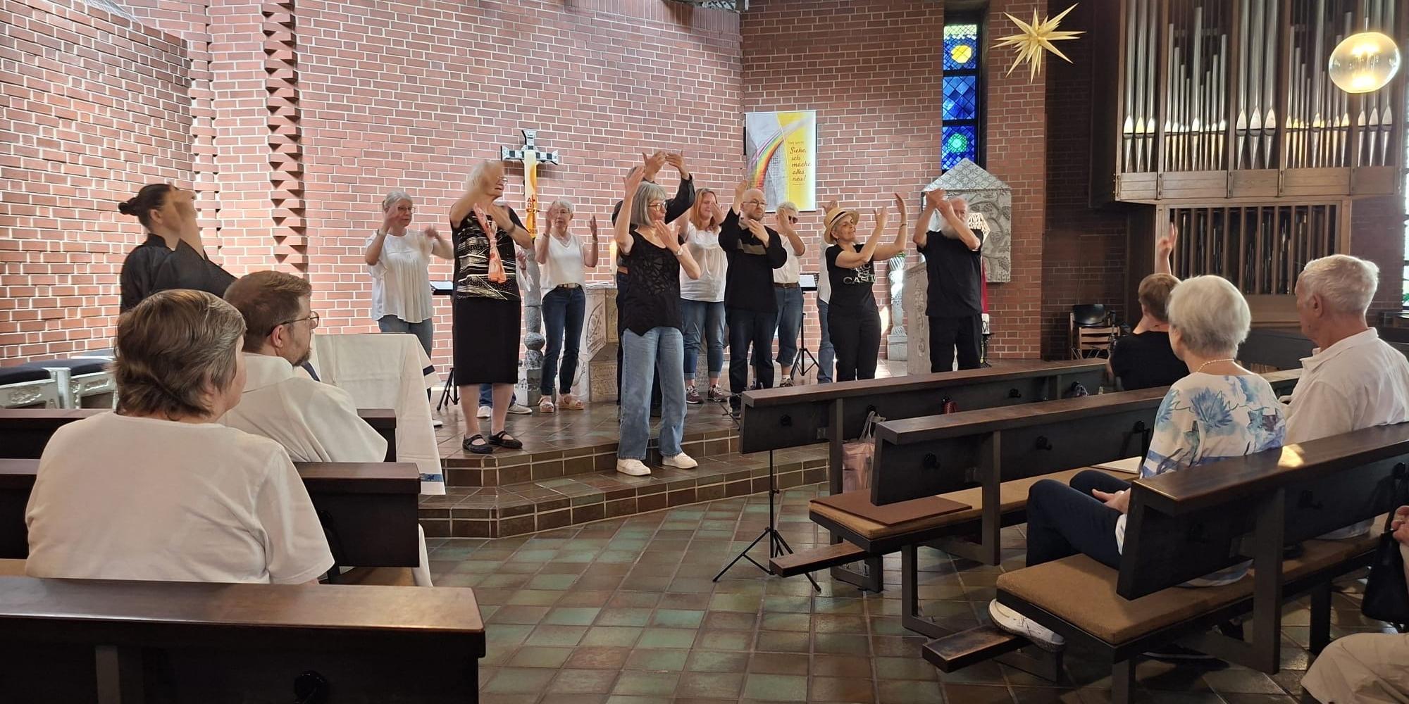 Gruppe führt vor der Gemeinde ein Lied in Gebärdensprache im Altarraum einer Kirche auf.