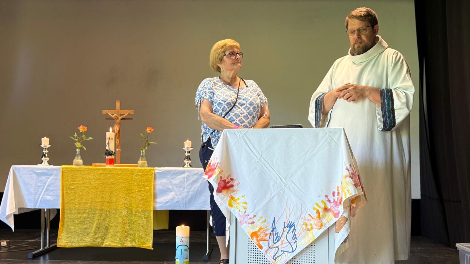 Zwei Mitwirkende stehen am Lesepult; Altar, Kerzen und Kreuz sind im Hintergrund zu sehen.