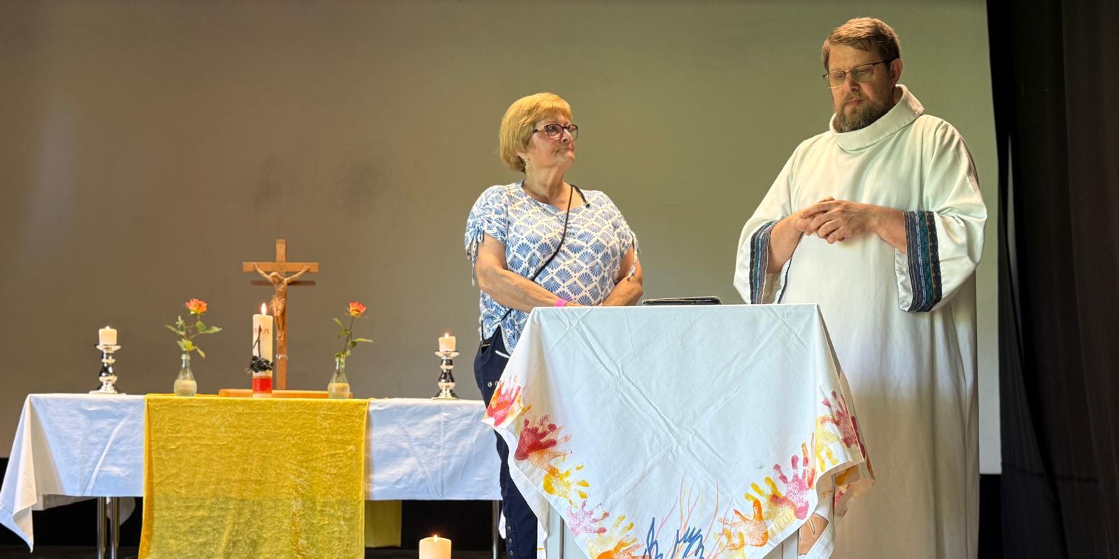 Zwei Mitwirkende stehen am Lesepult; Altar, Kerzen und Kreuz sind im Hintergrund zu sehen.