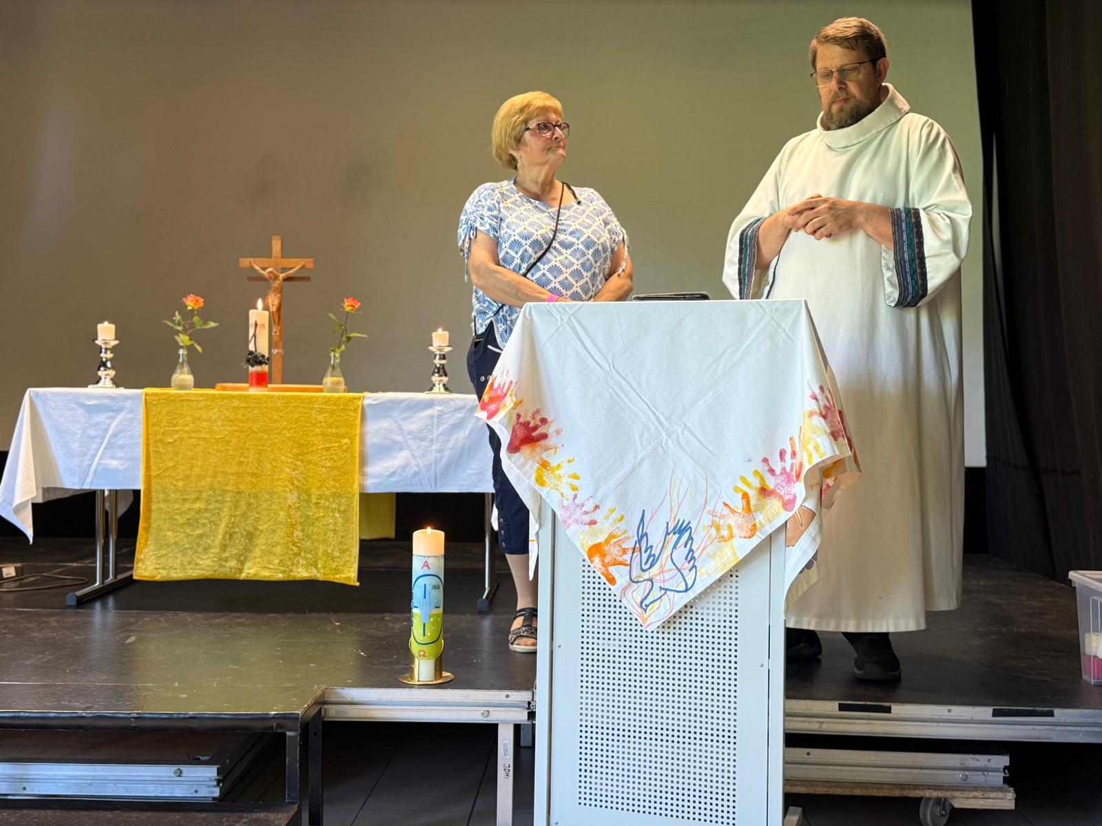 Zwei Mitwirkende stehen am Lesepult; Altar, Kerzen und Kreuz sind im Hintergrund zu sehen.